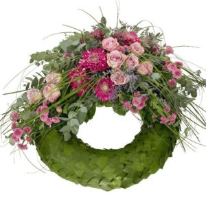Begravningskrans med själva stommen i grönt, på toppen en dekoration med anastasia, rosor, santini och gröna strån. Blommor i lila/cerise. Begravningskransen finns att beställa online hos Interflora.