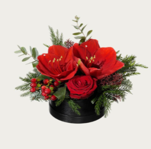 Rund hattask med låg juldekoration. Röd amaryllis, röd ros, hypericum och dekorationsgrönt. Juldekorationen finns att beställa som blommogram hos Interflora.